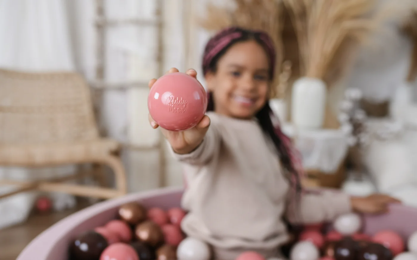 Child holding a KiddyMoon plastic ball above a ball pit