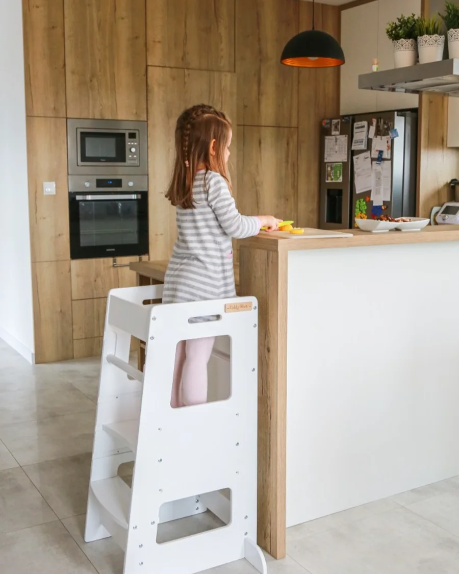 Girl on a white KiddyMoon learning tower in a modern kitchen