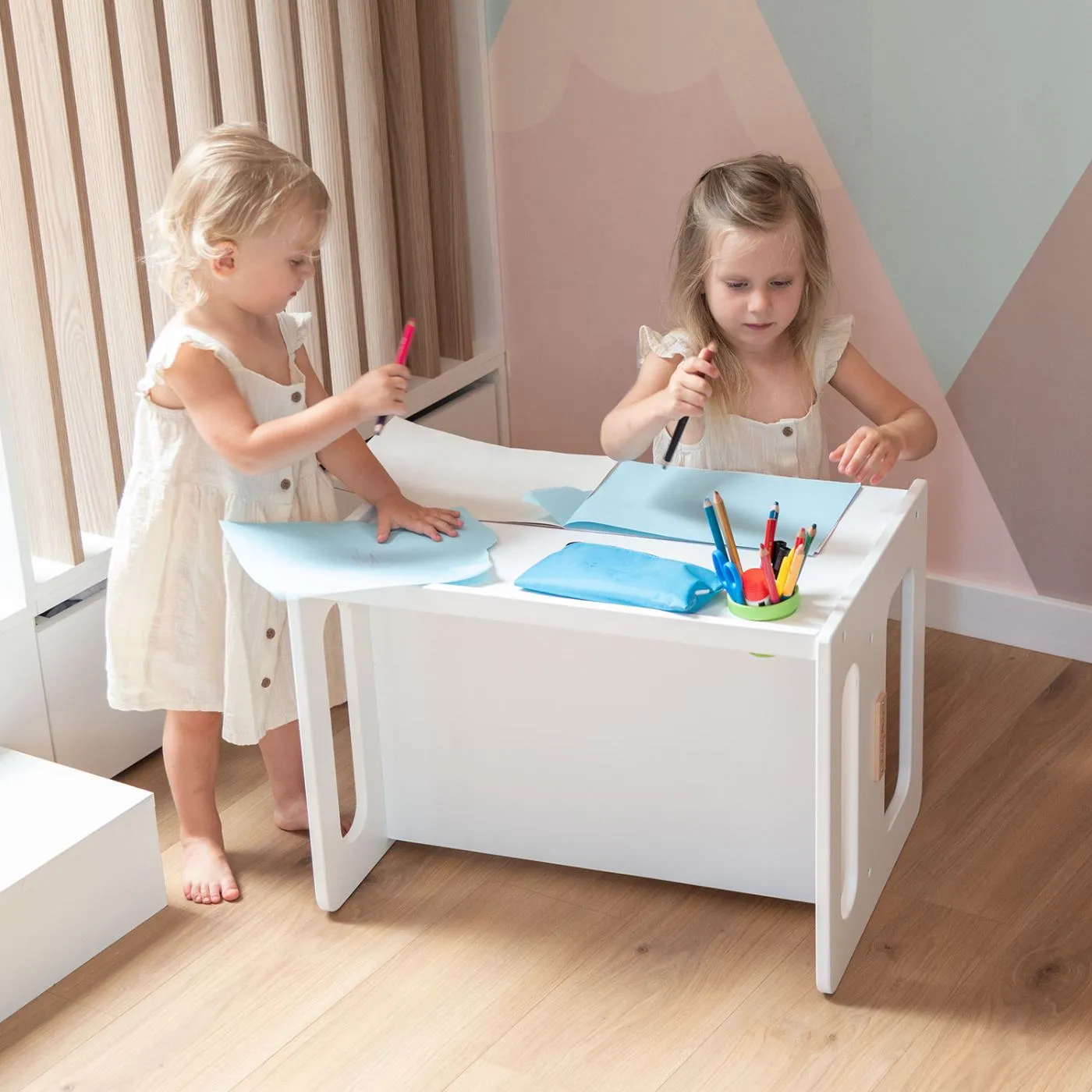 Two girls at a white KiddyMoon children's table in a bright nursery
