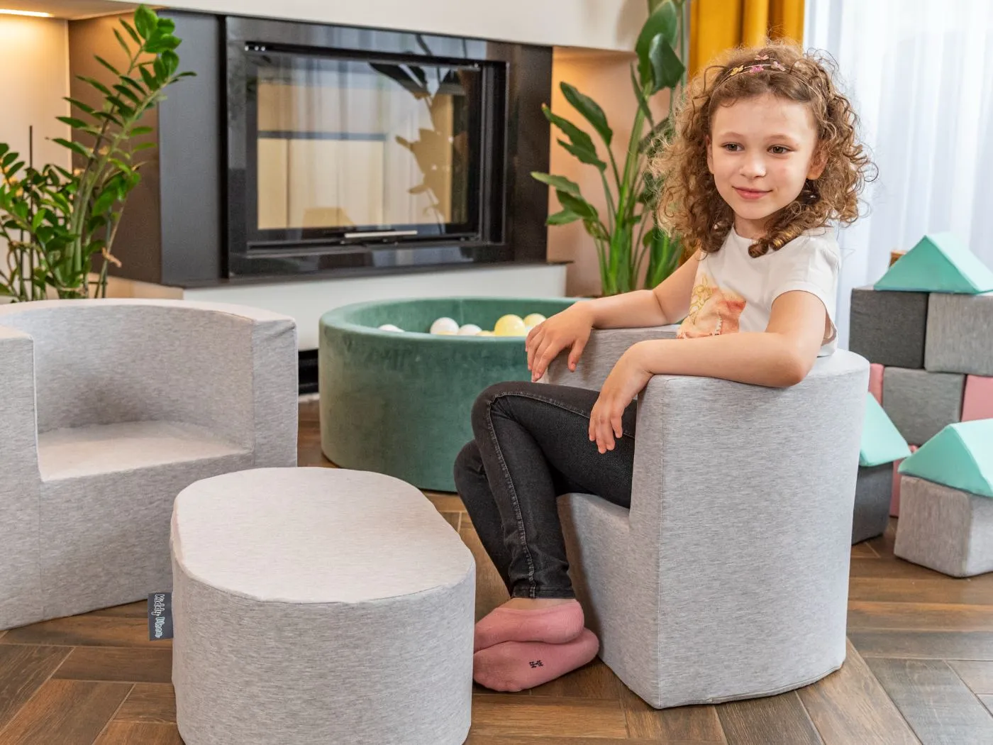 Girl sitting on a grey foam armchair with matching footstool in a living room