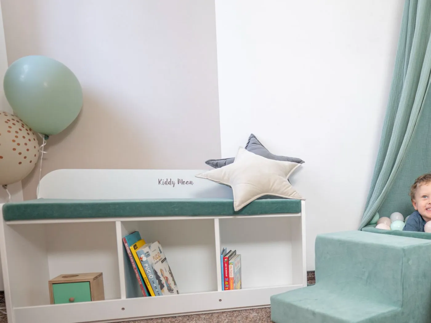 White KiddyMoon storage bench with open shelves for picture books and a green velvet cushion